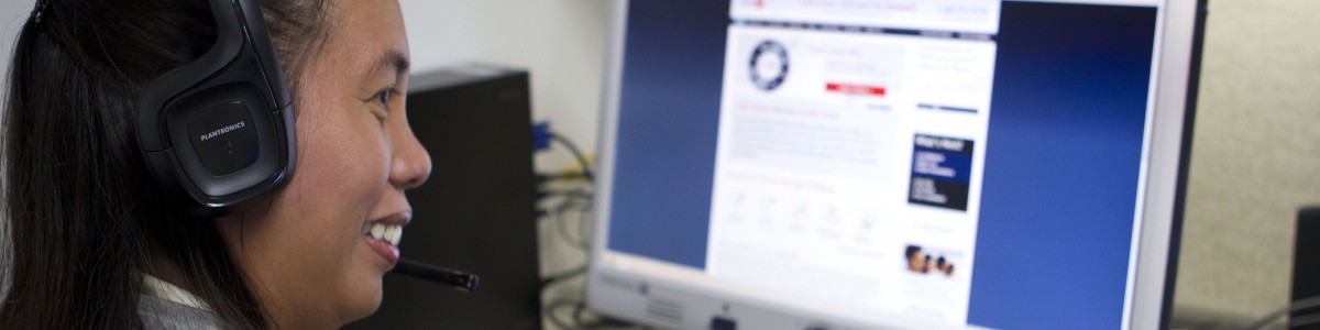 A woman wearing headphones uses her keyboard to navigate her computer screen