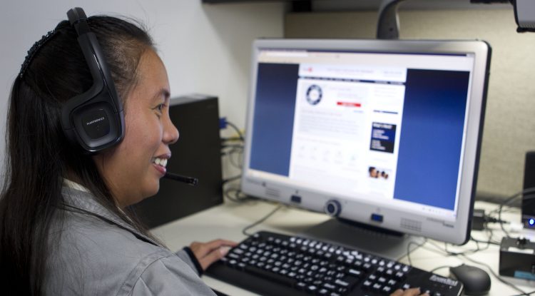 A woman wearing headphones uses her keyboard to navigate her computer screen