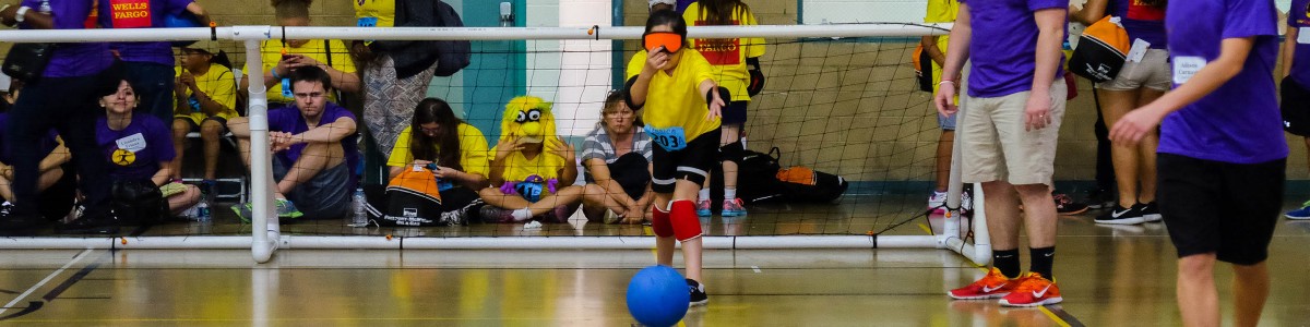 A girl wearing a blindfold throws a blue goalball across a court