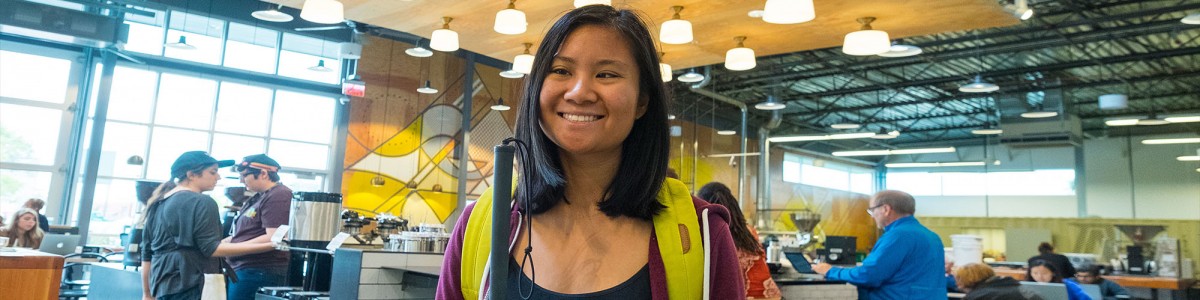 A young lady holding a cane smiles at the camera