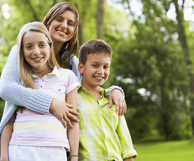 A mother wraps her arms lovingly around a young boy and girl.