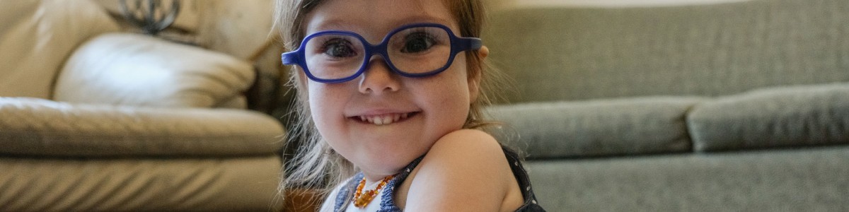 A toddler wearing glasses smiles at the camera.