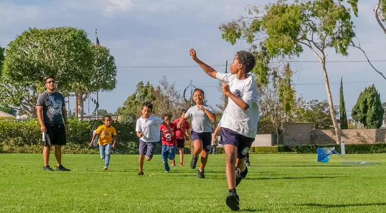 A young boy runs with a kite, with a group of children behind him