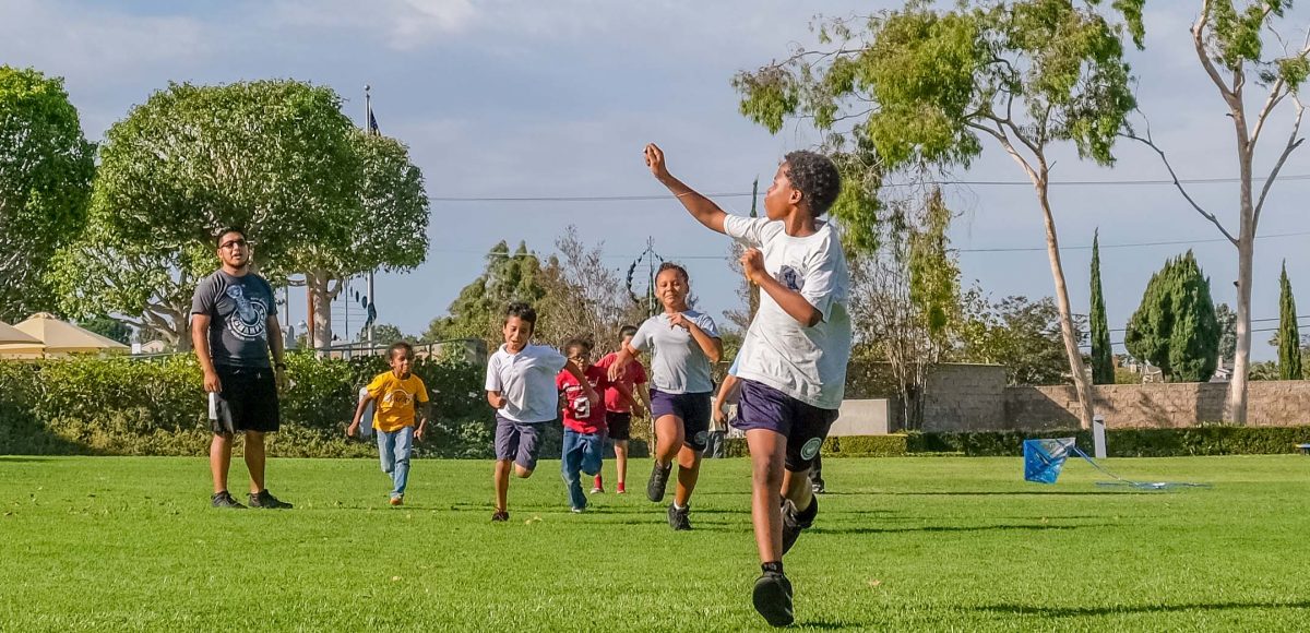 A young boy runs with a kite, with a group of children behind him