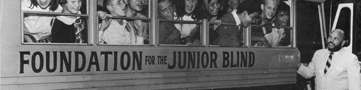 Norm Kaplan stands outside the door of a school bus that reads Foundation for the Junior Blind, smiling fondly at the children leaning out the windows.