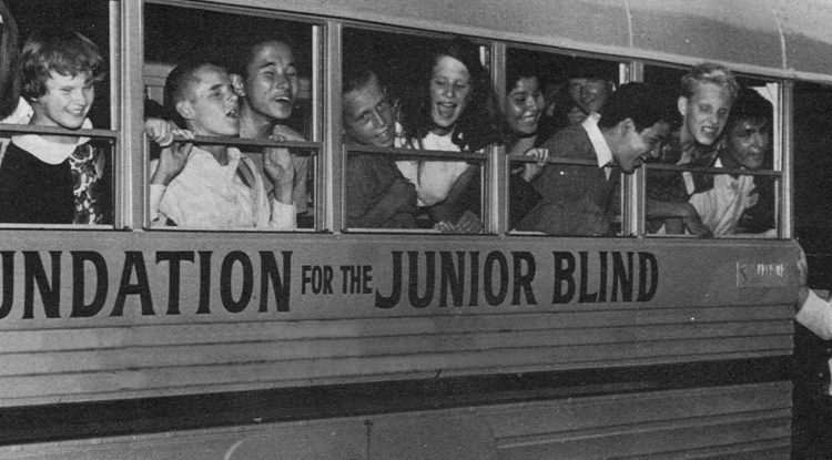 Norm Kaplan stands outside the door of a school bus that reads Foundation for the Junior Blind, smiling fondly at the children leaning out the windows.