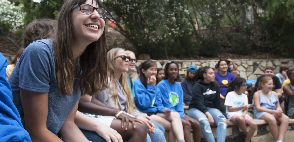 Paloma closes her eyes and smiles while sitting at the campfire circle with her friends at Camp Bloomfield