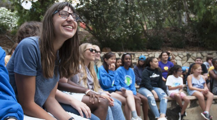 Paloma closes her eyes and smiles while sitting at the campfire circle with her friends at Camp Bloomfield