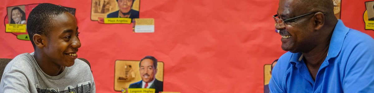 A young man sits in front of a bulletin board with a counselor