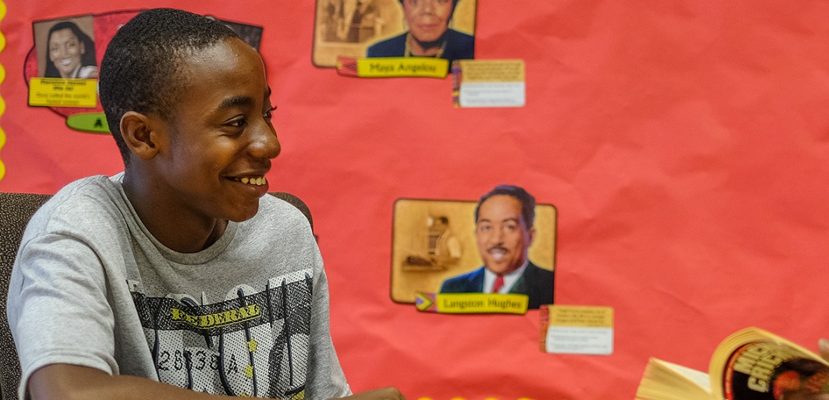 A young man sits in front of a bulletin board with a counselor