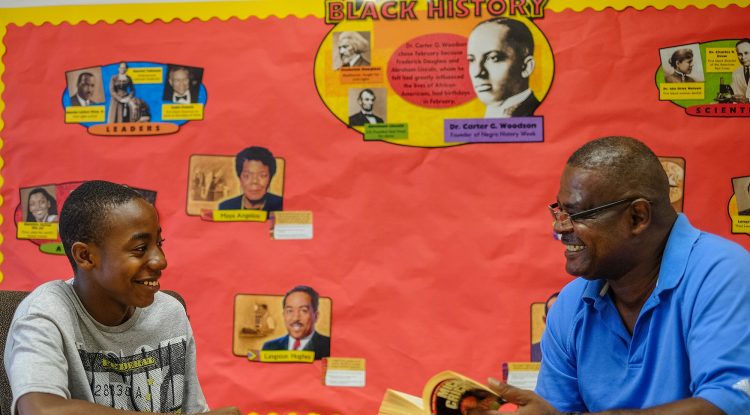 A young man sits in front of a bulletin board with a counselor