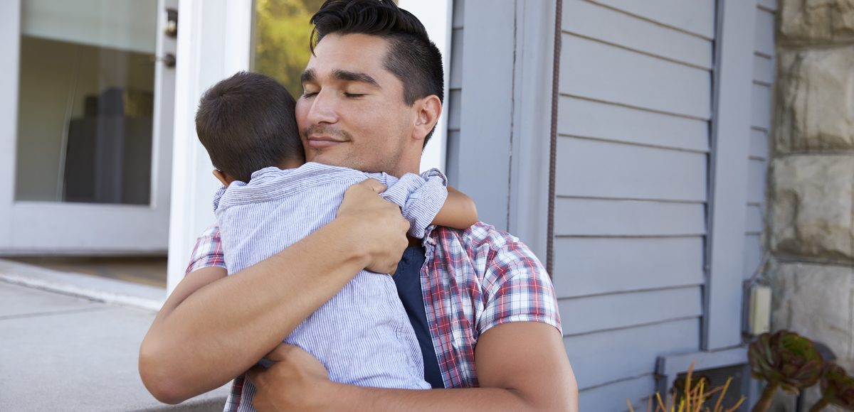 Father Hugging Son Sitting On Steps Outside Home