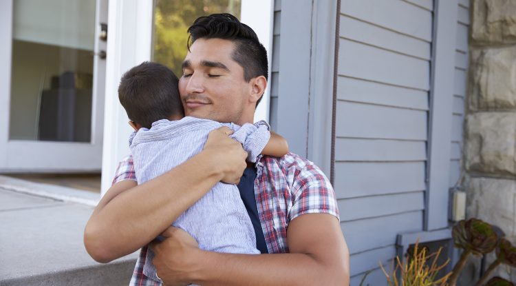 Father Hugging Son Sitting On Steps Outside Home