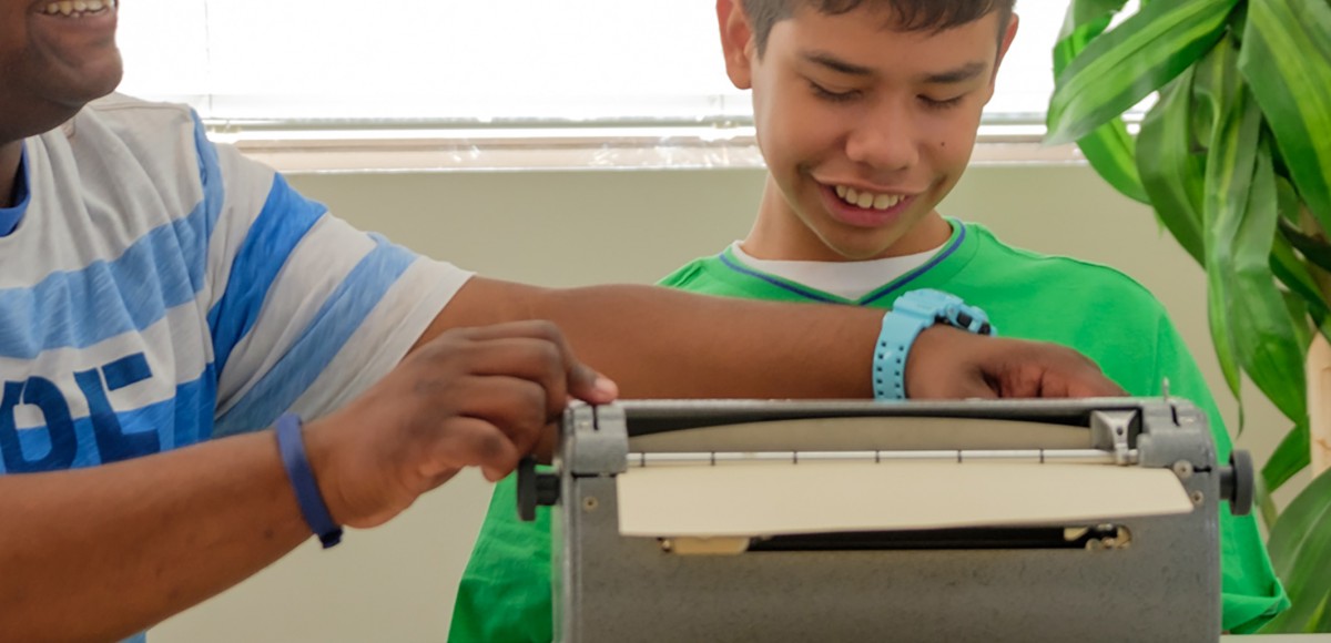 An instructional aide assists a young boy who is blind with a Brailler.