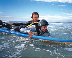 An instructor assists a Junior Blind student on a surfboard during a Visions Adventures trip