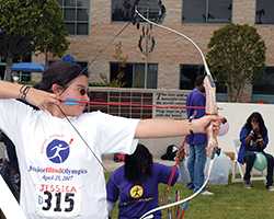 A child who is visually impaired pulls back an arrow on a bow during the Junior Blind Olympics