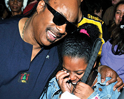 Stevie Wonder smiles next to a student who is holding a white cane