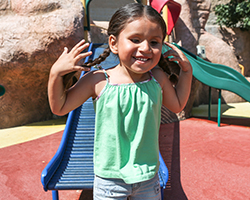 A child smiles on the campus of Junior Blind in front of a slide