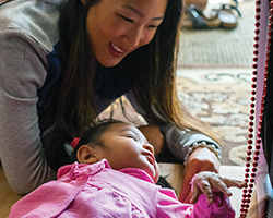 A visual impairment specialist looks down at a baby who is gazing off in the distance