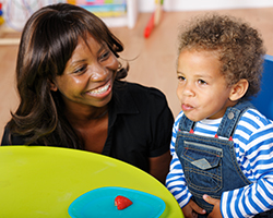 A caregiver smiles as she helps a young boy eat fruit