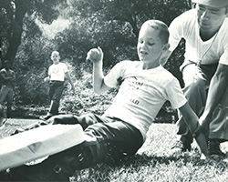 A young boy slides into a base, assisted by a counselor, during a game at Camp Bloomfield