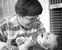 A father gazes down at his toddler in his arm. Both are smiling.