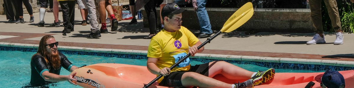 A young boy who is visually impaired paddles a kayak, guided by two volunteers at the Wayfinder Paralympic Games
