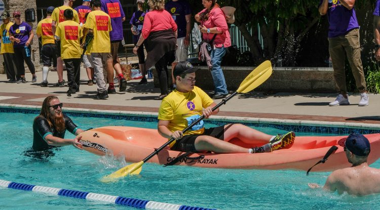 A young boy who is visually impaired paddles a kayak, guided by two volunteers at the Wayfinder Paralympic Games