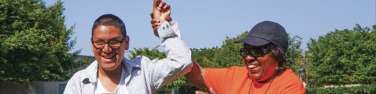 A volunteer holds the hand of a smiling student high in the air