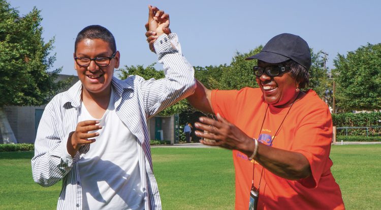 A volunteer holds the hand of a smiling student high in the air