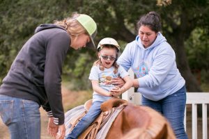 Staff helping child ride a horse at camp