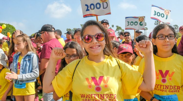 girl raising her arms and smiling at wayfinder paralympics