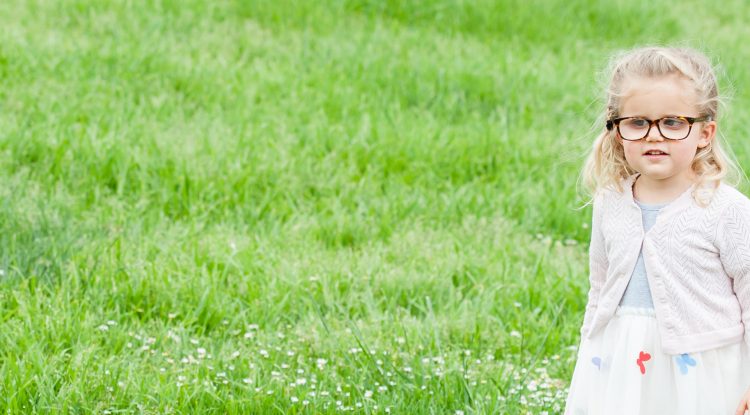 Smiling little girl wearing glasses and holding white cane