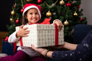 little girl with big gift under holiday tree