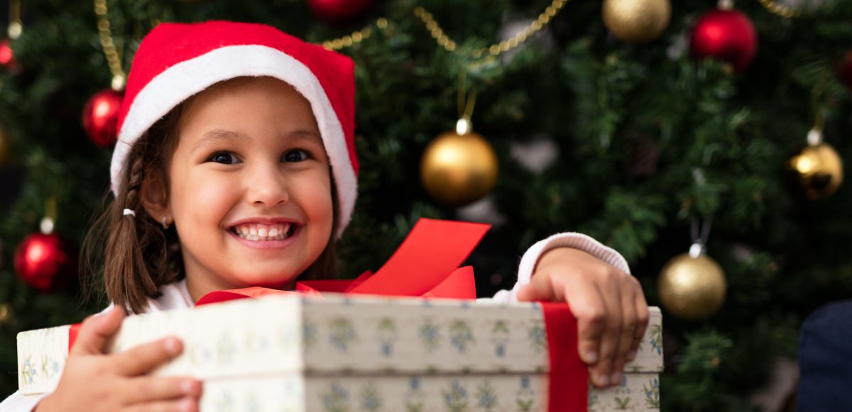 little girl with big gift under holiday tree