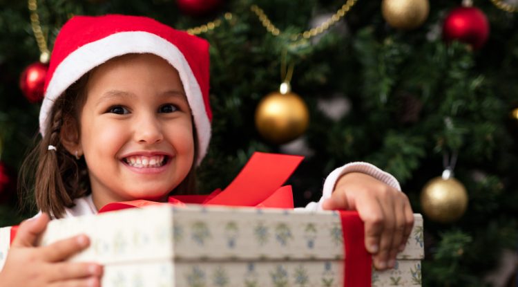 little girl with big gift under holiday tree