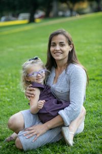 child with glasses smiles while sitting on her mom's lap