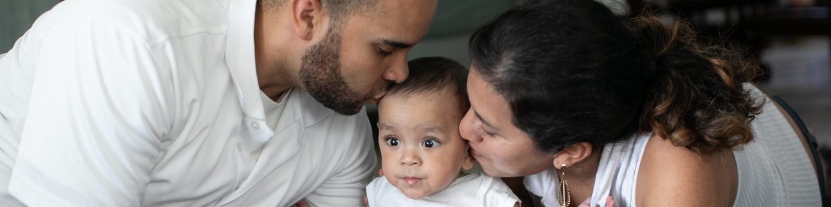 father and mother kiss their baby who is sitting in between them.