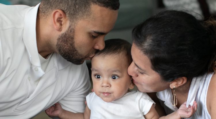 father and mother kiss their baby who is sitting in between them.