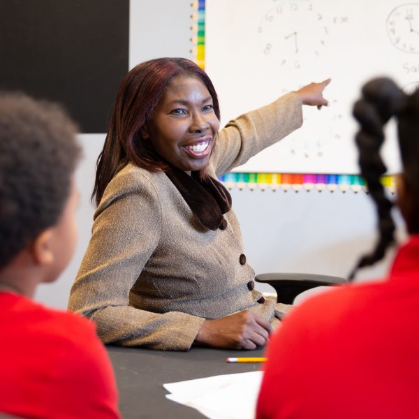 smiling woman points to white board as students watch