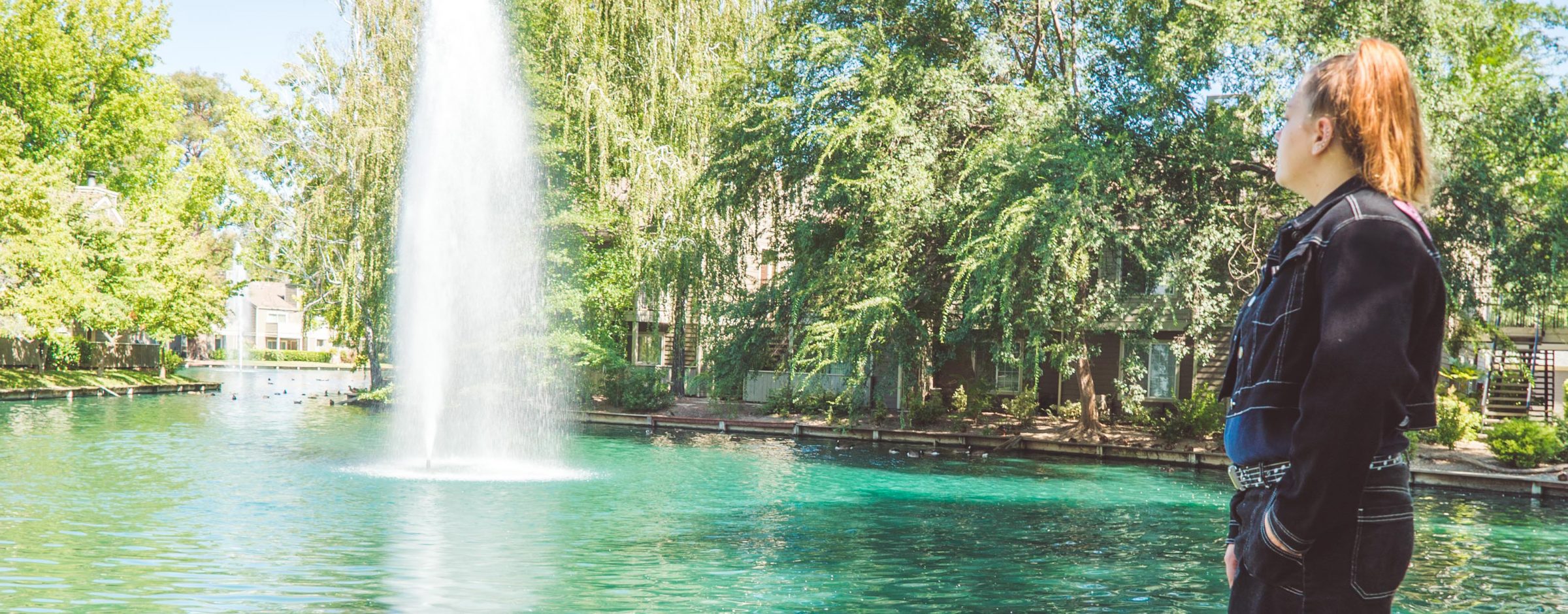 young woman standing on grass and looking at fountain