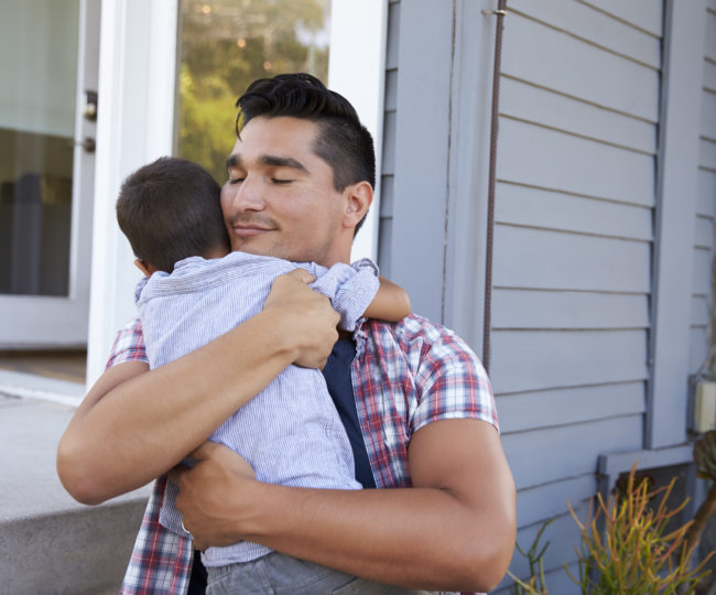 Father Hugging Son Sitting On Steps Outside Home