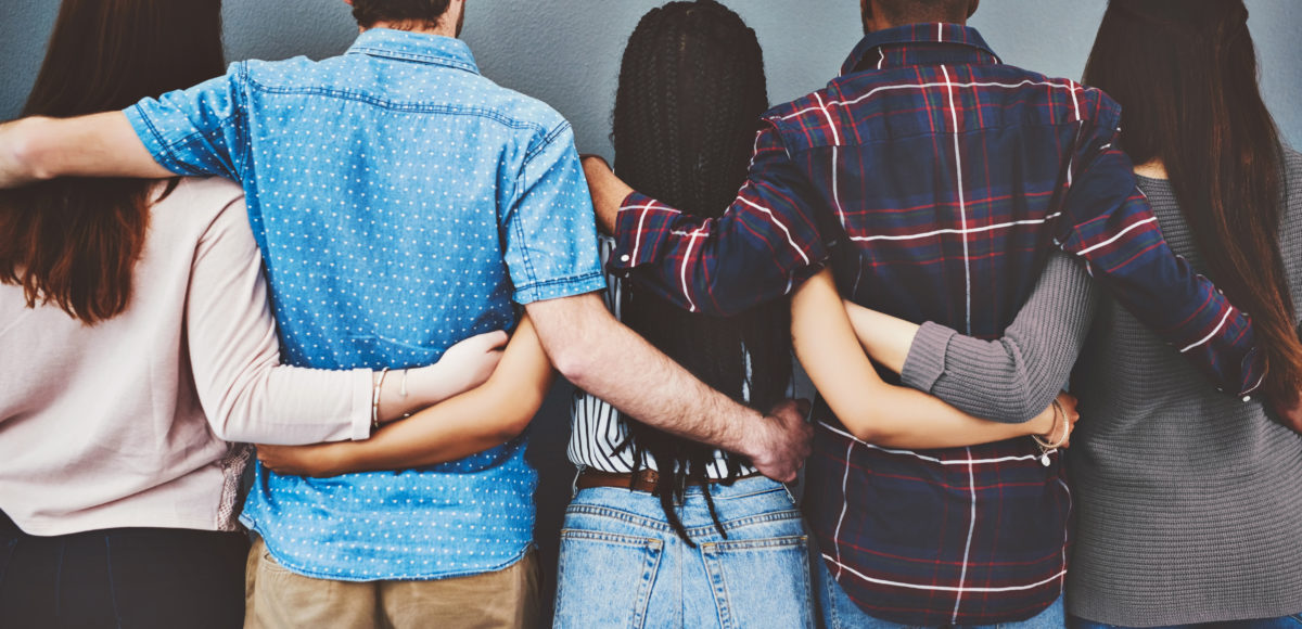 Rearview studio shot of a group of young people standing together and embracing