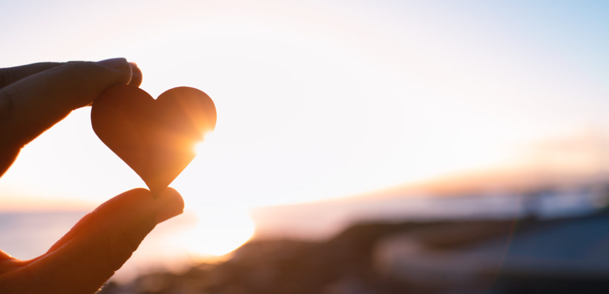 hand holding up small heart shaped stone against sunrise