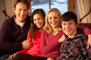 family of four smiling at camera. dad, teen daughter, mom and teen son
